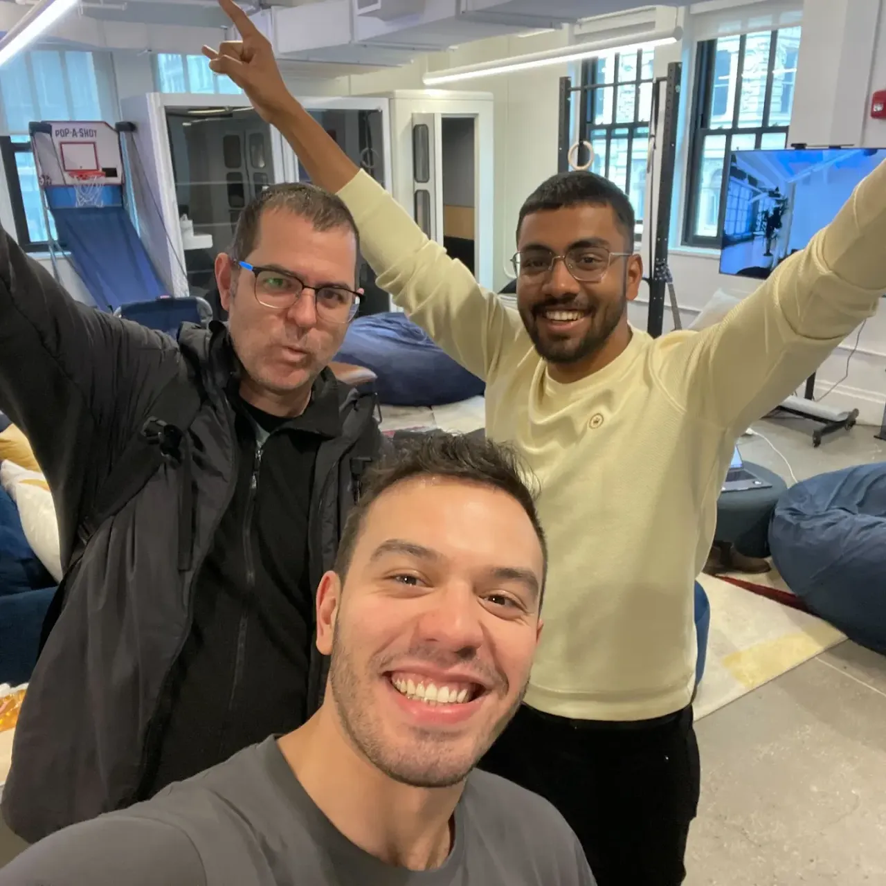 Three people grinning with their arms in the air in an open-plan office.